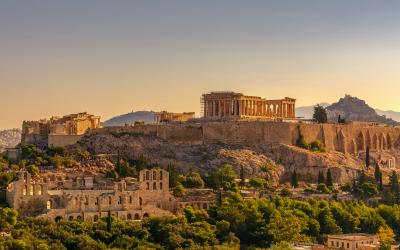 A view of the Acropolis of Athens, featuring the Parthenon and other ruins on the rock, with the Lycabettus hill visible in the background.