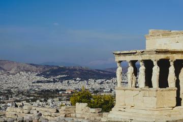 The image shows the Porch of the Caryatids on the Acropolis in Athens, Greece, overlooking the city of Athens and the surrounding hills.