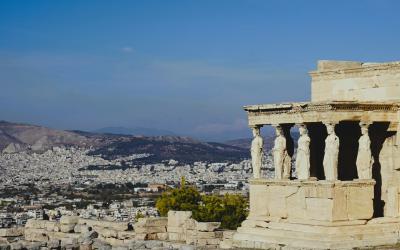 The image shows the Porch of the Caryatids on the Acropolis in Athens, Greece, overlooking the city of Athens and the surrounding hills.