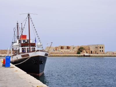 A black and white boat named "RINI" is moored at a stone pier in a harbor, with historic stone fortifications and buildings visible in the background.