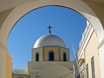 A view through a white archway of a yellow and blue Orthodox church dome topped with a cross against a clear blue sky.