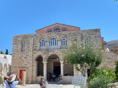 A large, historic stone church with a distinctive facade featuring three arched windows on the upper level and a central arched entrance supported by columns, set against a clear blue sky with tourists present.