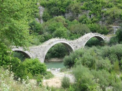 The triple-arched Kalogeriko (Plakidas) stone bridge near Kipi in Zagori, Epirus, spanning a green river among wooded limestone slopes