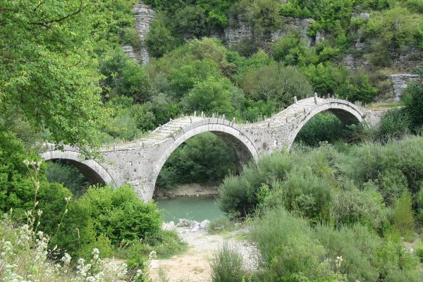 The triple-arched Kalogeriko (Plakidas) stone bridge near Kipi in Zagori, Epirus, spanning a green river among wooded limestone slopes