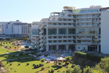 A large, modern white hotel complex with distinctive spiral staircases and multiple swimming pools set within landscaped gardens.