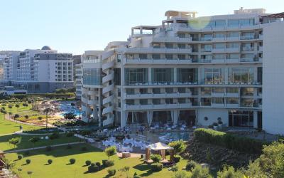 A large, modern white hotel complex with distinctive spiral staircases and multiple swimming pools set within landscaped gardens.