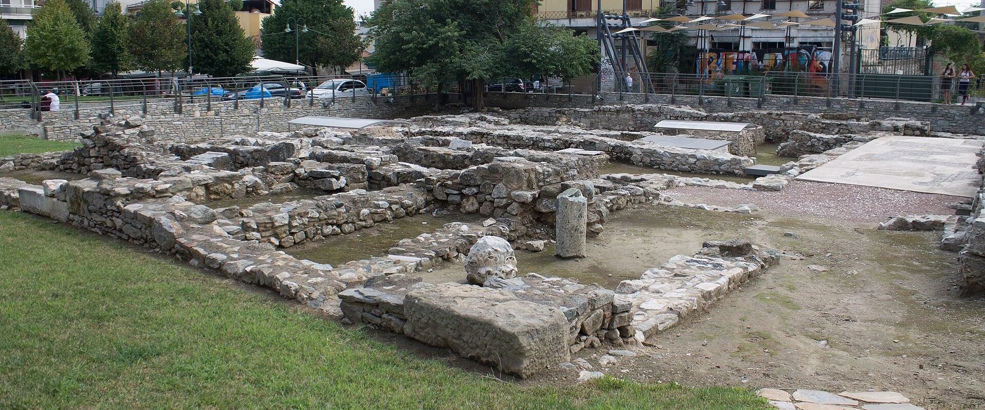 The image shows a close-up of a stone sarcophagus or tomb structure within an archaeological excavation site, partially covered by a modern metal protective shelter.