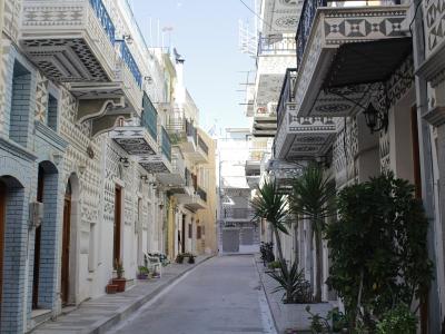 A narrow street in a village featuring buildings with distinctive black and white geometric patterns (xysta) on the facades and balconies.