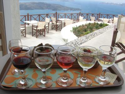 A wine tasting flight of five glasses on a tray with a view of the caldera and sea from a terrace.