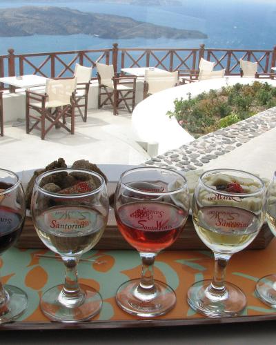 A wine tasting flight of five glasses on a tray with a view of the caldera and sea from a terrace.