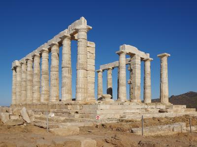 The image shows the ancient ruins of a Doric temple with standing columns and a partial entablature, situated on a rocky coastal promontory under a clear blue sky.