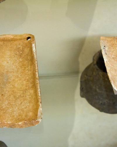 A close-up photograph of two ancient marble artifacts, identified as Cycladic "palettes," displayed inside a glass museum case on supports.