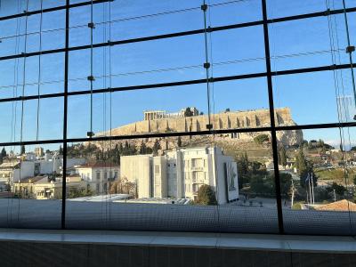 A view through the large glass windows of a modern building looking out towards the Acropolis hill and the Parthenon in Athens, Greece.