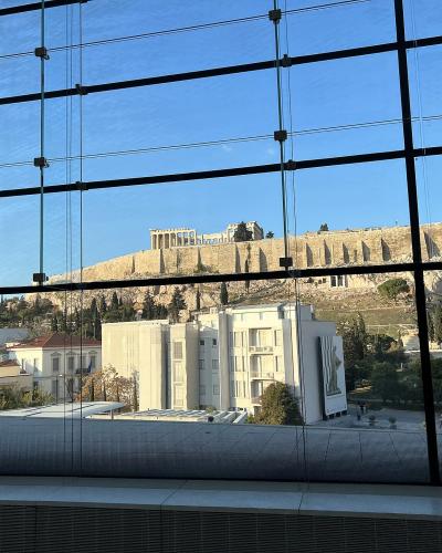 A view through the large glass windows of a modern building looking out towards the Acropolis hill and the Parthenon in Athens, Greece.