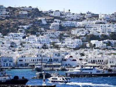 A view of a harbor filled with boats and ferries, with a dense hillside of white-washed buildings rising behind the waterfront.