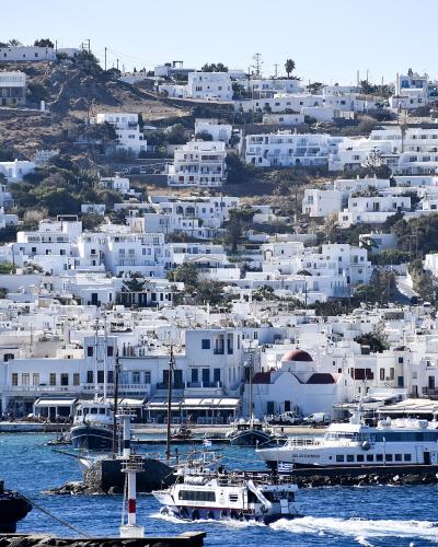 A view of a harbor filled with boats and ferries, with a dense hillside of white-washed buildings rising behind the waterfront.