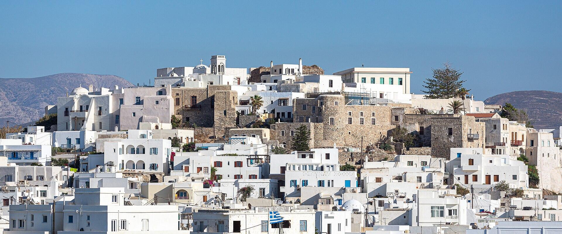 A view of the white-washed buildings and stone fortifications of Naxos Chora, seen through the gaps of a stone wall in the foreground.
