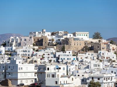 A view of the white-washed buildings and stone fortifications of Naxos Chora, seen through the gaps of a stone wall in the foreground.