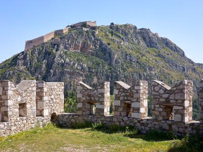 A view from the battlements of a stone fortress looking up a steep, rocky hill towards a larger fortification structure at the summit.