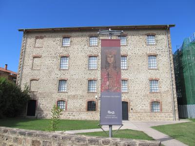 A large, three-story stone building with a grid of arched windows, featuring a vertical banner in the foreground displaying a Byzantine icon and Greek text.