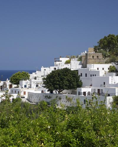 A coastal view of a hillside village with whitewashed cubic houses leading up to a large ancient fortress on the summit, overlooking a sandy beach and turquoise sea.