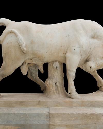 A marble sculpture of a bull rubbing its horns against a tree trunk, displayed on a stone plinth against a black background.