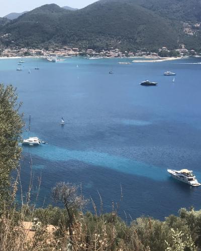 A high-angle view of a coastal bay with numerous boats anchored in blue water, a small town along the shoreline, and forested hills in the background.