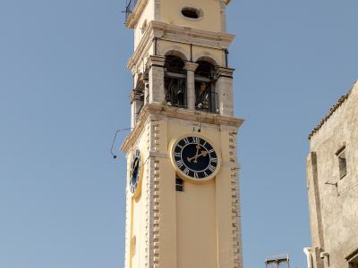 A low-angle shot of a tall, yellow-painted bell tower with stone quoins and a simple belfry opening against a clear sky.