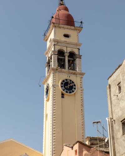 A low-angle shot of a tall, yellow-painted bell tower with stone quoins and a simple belfry opening against a clear sky.