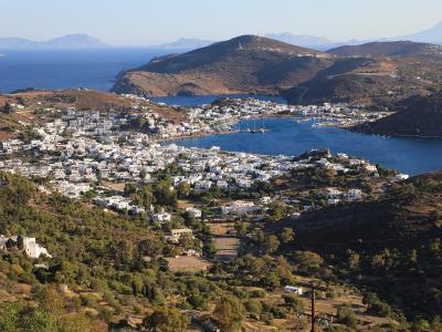 A panoramic view of a coastal town with white buildings clustered around a harbor, seen from an elevated position with windmills in the foreground.