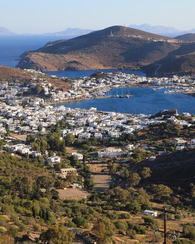 A panoramic view of a coastal town with white buildings clustered around a harbor, seen from an elevated position with windmills in the foreground.