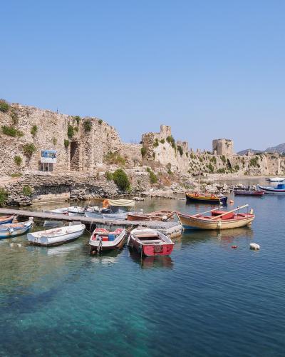 A view of a historic stone fortress wall running along a harbor filled with small fishing boats and yachts under a clear blue sky.