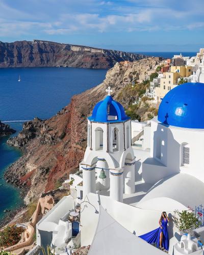 A high-angle view of the iconic blue-domed churches of Oia on the cliffs of Santorini, overlooking the volcanic caldera and the Aegean Sea.