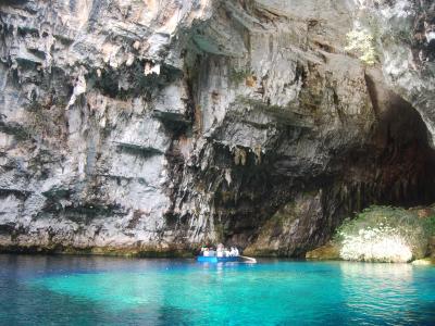 A boat carrying tourists on turquoise water inside a large limestone cave with a collapsed ceiling opening and visible stalactites.