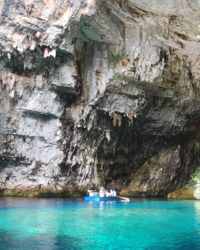 A boat carrying tourists on turquoise water inside a large limestone cave with a collapsed ceiling opening and visible stalactites.