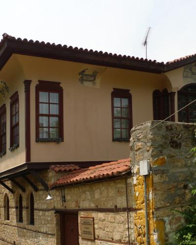 A two-story building with a stone ground floor and a stucco upper floor featuring dark wood window frames and decorative elements, with a small plaque mounted on the stone wall near the entrance.