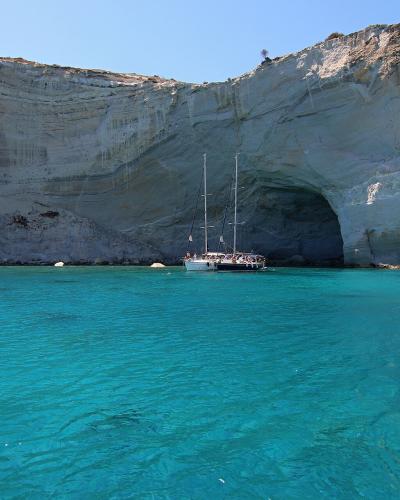 A view of a large, white limestone cliff face with a prominent natural archway and sea caves, with a tour boat anchored in the turquoise water in front.