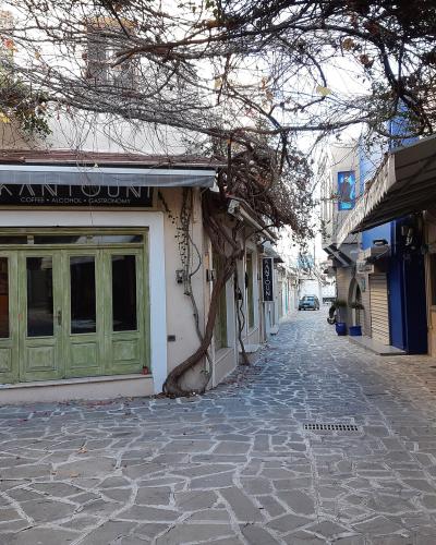 A narrow, cobblestone pedestrian street in a town, featuring a cafe named "KANTOUNI" on the left and a scooter parked on the right, with vines overhead.