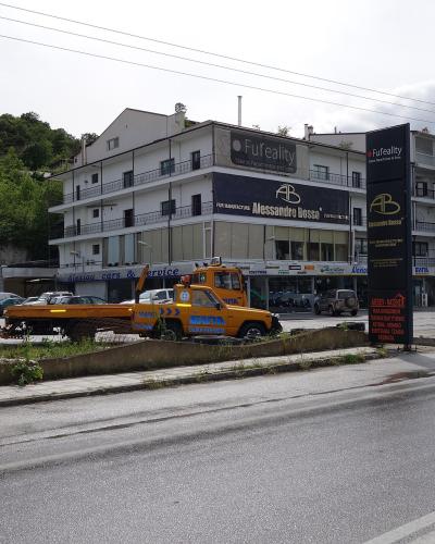 A street-level view of a multi-story white building with a large black sign reading "Fuf reality" and "ALESSANDRO BOSSO" on the facade, alongside a tow truck in the foreground.