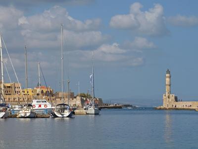 A view of a harbor with numerous sailboats docked on the left and a distinctive stone lighthouse situated at the end of a long breakwater on the right.