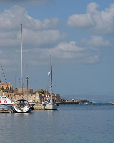 A view of a harbor with numerous sailboats docked on the left and a distinctive stone lighthouse situated at the end of a long breakwater on the right.