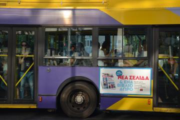 A side view of a purple and yellow public transit bus with passengers visible through the windows and an advertisement on the side panel.