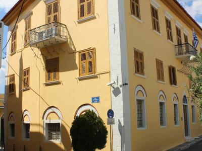 A yellow neoclassical building with brown shutters, white corner quoins, and a Greek flag, identified by the filename as the Benakeio Archaeological Museum of Kalamata.