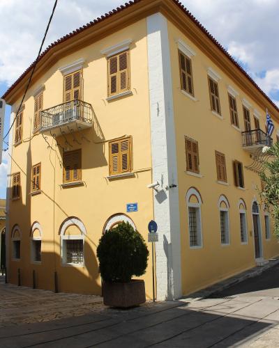 A yellow neoclassical building with brown shutters, white corner quoins, and a Greek flag, identified by the filename as the Benakeio Archaeological Museum of Kalamata.