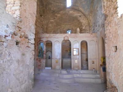 The interior of a ruined stone church featuring a brick-vaulted ceiling, an iconostasis with religious icons, and rough masonry walls.