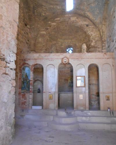 The interior of a ruined stone church featuring a brick-vaulted ceiling, an iconostasis with religious icons, and rough masonry walls.