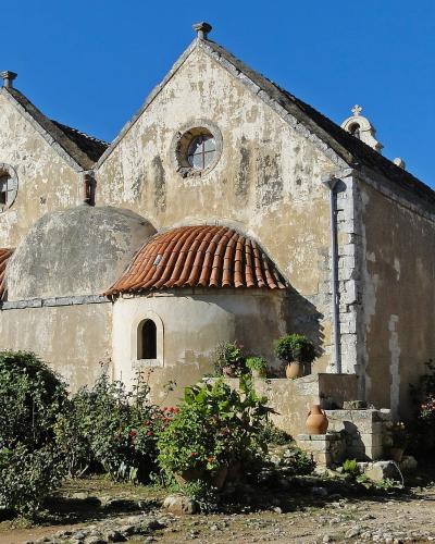 The image shows the rear exterior of a historic stone church featuring a central dome, two smaller apses with terracotta tile roofs, and circular windows set against a clear blue sky.
