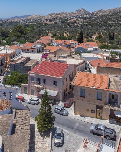 An elevated view of a Greek village with terracotta-roofed buildings, a white church with a dome and bell tower in the foreground, and a backdrop of olive groves and hills.