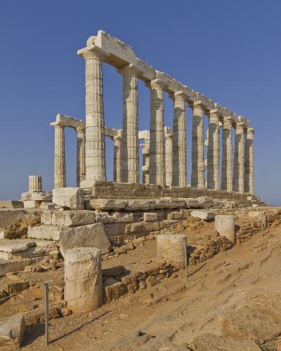 The image shows the ruins of the Temple of Poseidon at Cape Sounion, featuring its iconic Doric columns against a clear blue sky.