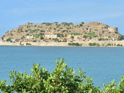 A paved pathway winding through the stone ruins of an abandoned settlement with arid hills in the background under a blue sky.
